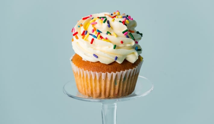 Imagem de um cupcake em forma branca decorado com chantily branco e granulados coloridos.
