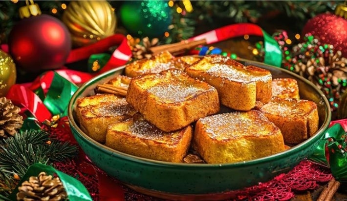 Em cima de uma mesa com bolinhas e pinhas de natal, prato com rabanadas, polvilhadas com açúcar de confeiteiro.