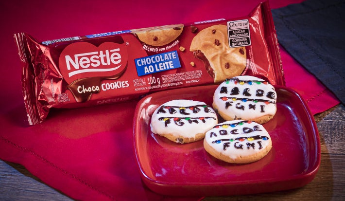 Cookies redondos cobertos com chocolate branco, decorados com luzinhas coloridas e letras feitas em chocolate escuro, lembrando um varal iluminado.