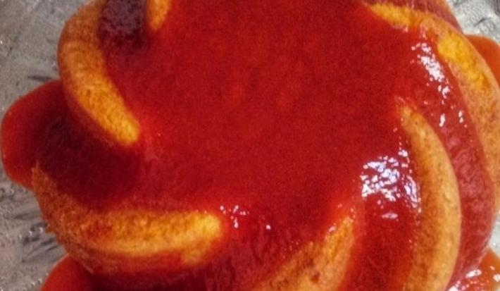 Fotografia em tons de vermelho em uma bancada de madeira de cor cinza. Ao centro, um prato transparente contendo o bolo de fubá.