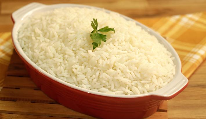 Foto de um recipiente vermelho com arroz branco dentro e uma folha de coentro decorando