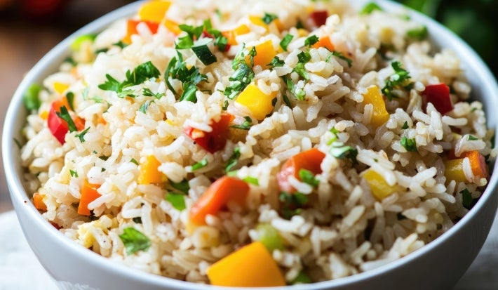 Em cima de uma mesa, tigela redonda com porção de arroz soltinho com pimentões amarelo, vermelho, ervilhas e cenouras picadas.