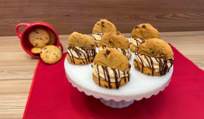 Fotografia mostra cookies cobertos por um creme branco e chocolate derretido, e meio cookie no topo.
