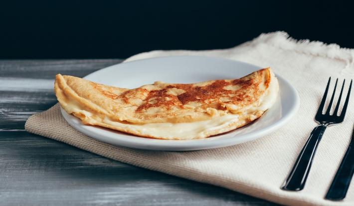 Foto aproximada da receita de Crepioca de Aveia em Flocos, em um prato branco, sobre um tecido em tom bege, com dois talheres de metal ao lado.