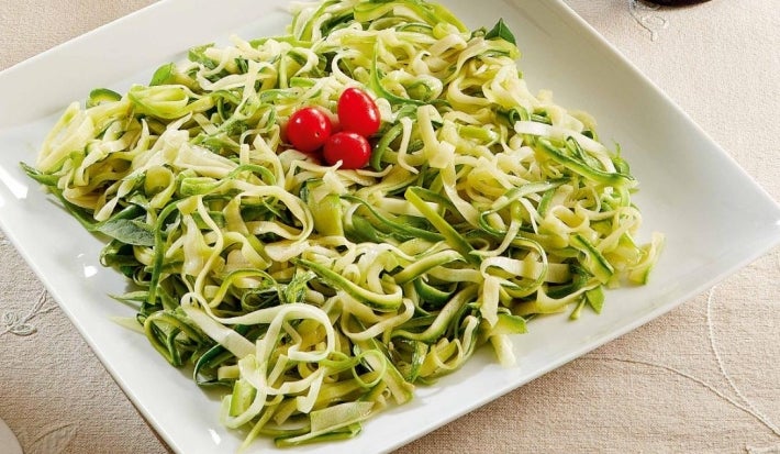 Prato quadrado branco com macarrão de abobrinha em tiras com manjericão decorado com tomates cereja.