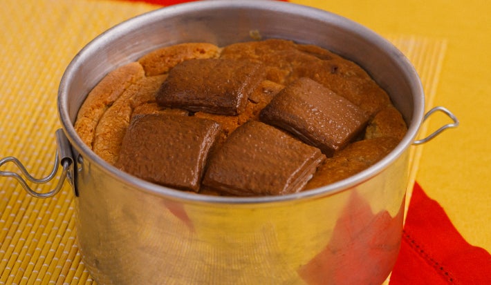 Cookie gigante assado em lata metálica, com pedaços de chocolate Baton sobre a massa dourada.