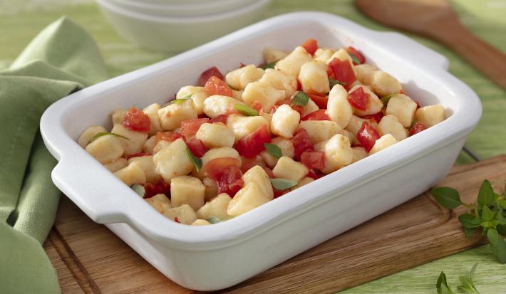Foto da receita de Nhoque sem Glúten. Observa-se um refratário retangular branco com o nhoque dentro ao molho de tomate, decorado com folhas de manjericão.