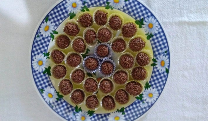 Fotografia vista de cima de várias unidades de brigadeiro enrolados e passados no granulado sobre um prato colorido, raso.