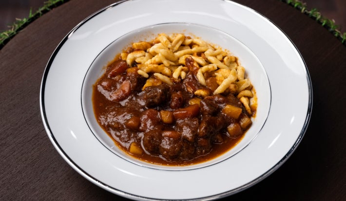 Goulash com molho escuro, carne cozida lentamente e spätzle salteado no prato branco