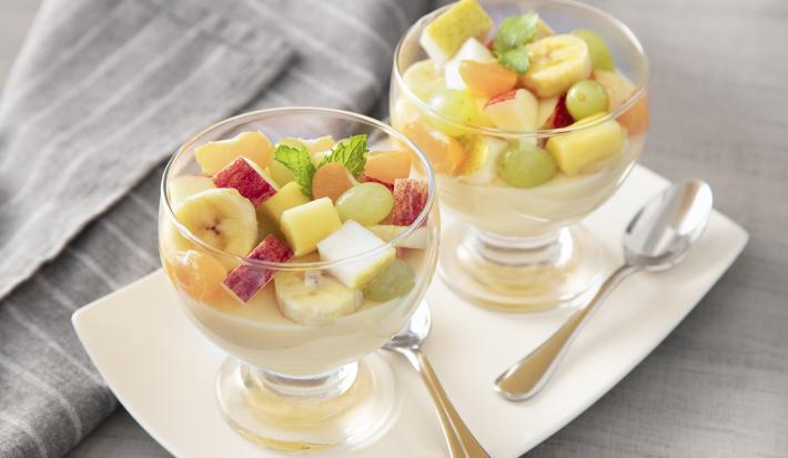 Receita de Gelatina de Frutas. Observa-se duas taças de vidro individuais sobre uma tábua branca e com gelatinas e frutas cortadas dentro.