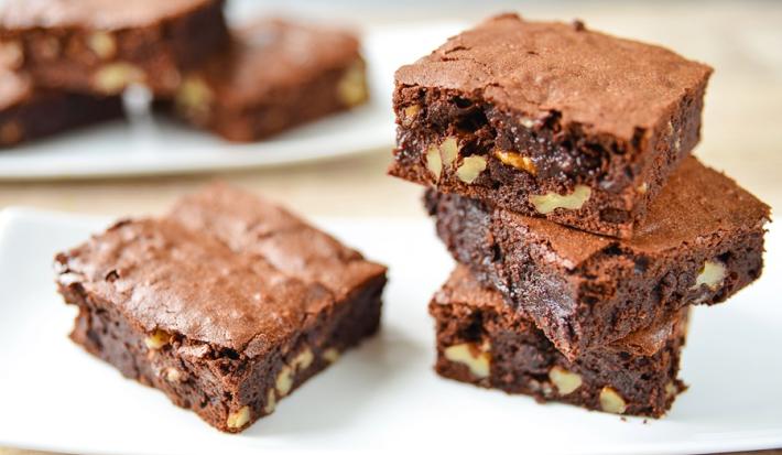 Imagem de três pedaços quadrados de brownie empilhados e um pedaço ao lado.