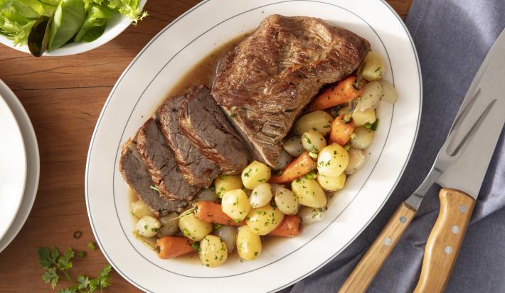 Imagem vista de cima de uma travessa oval branco com fatias de maminha e legumes (batatinha, cenoura e cebola).