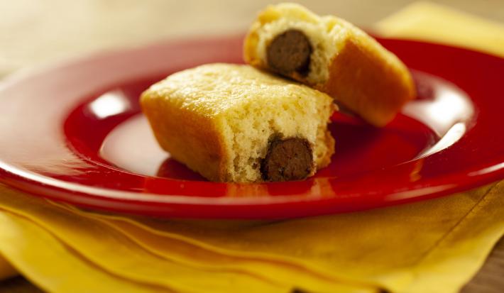 Fotografia em tons de vermelho e amarelo de uma bancada de madeira com um paninho amarelo e sobre ele um prato vermelho com dois mini bolinhos recheados com um baton.