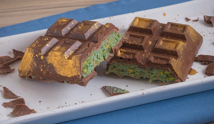 Barra de Dubai, receita de uma barra de chocolate recheada com um creme de pistache e macarrão, decorada com pó dourado e servida em um prato branco e cortada ao meio