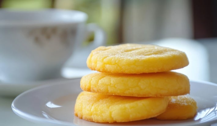 Em cima de uma mesa, prato branco redondo com biscoitos dourados e crocantes enfileirados.