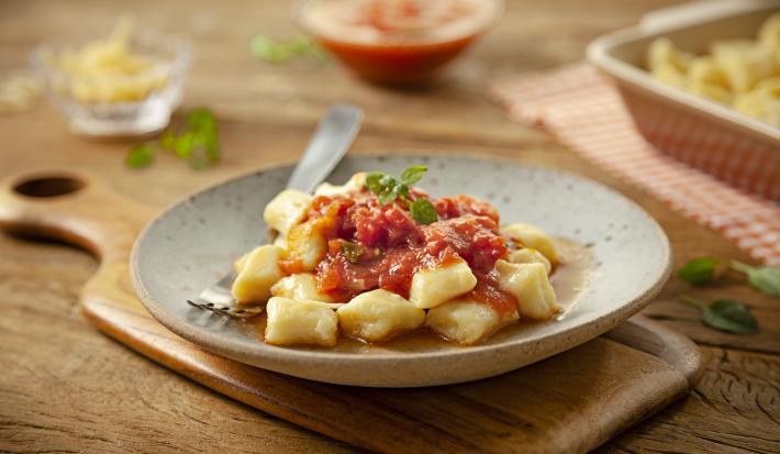 Imagem de um prato rústico com nhoque de batata com molho de tomate decorado com uma folha de manjericão.