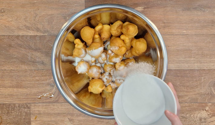 Bolinhos de chuva fritos dentro de bowl de inox sendo cobertos com açúcar e canela