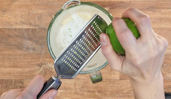 Mãos adicionando raspas de limão ao conteúdo do liquidificador