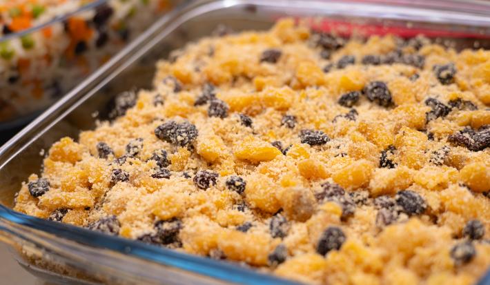 Fotografia de uma travessa de vidro quadrada com uma farofa de frutas deliciosa feita com farinha de mandioca com pêssego em calda, ameixa seca, uva-passa e MAGGI Fondor.