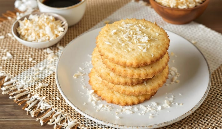 Em cima de uma mesa prato redondo, com biscoitos amanteigados enfileirados, decorado com coco ralado.