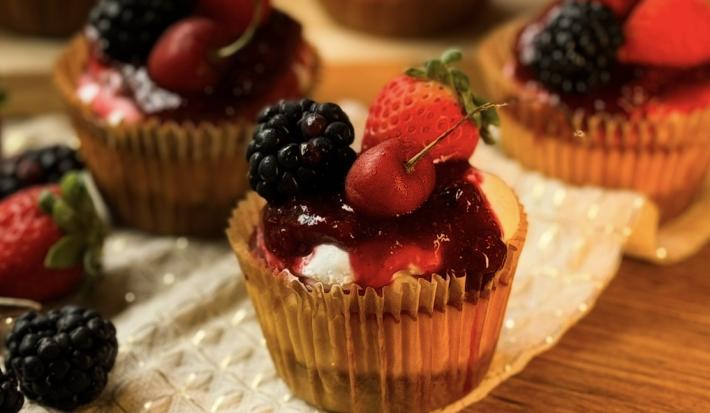 Fotografia de uma mini cheesecake com frutas vermelhas feita em uam forminha de papel de cupcake, ao fundo tem mais algumas.
