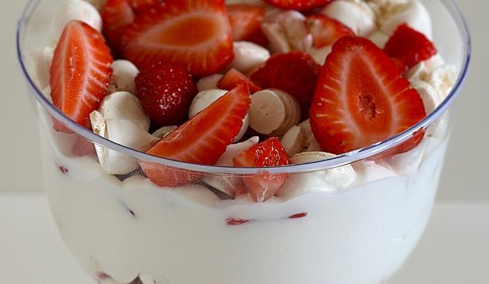 Fotografia de um recipiente decorativo fundo com uma receita de suspiro, creme e morangos em pedaços por cima.
