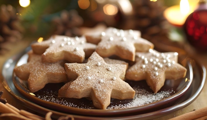 Em cima de uma mesa, biscoitos de estrelas, decorados com confeito prata de bolinha.