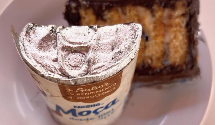 Fotografia de um bolo em formato de lata de leite moça. O bolo imita uma lata de Leite MOÇA e é recheado com ganache de maracujá e brigadeiro branco
