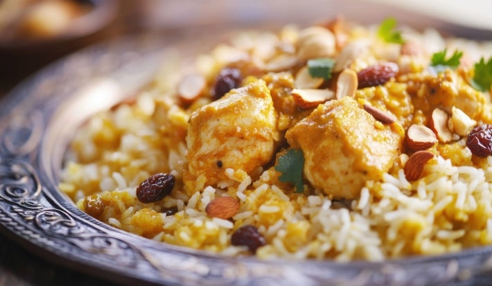 Um prato de Arroz Natal é apresentado em um prato, repleto de arroz soltinho e colorido. O arroz é misturado com pedaços suculentos de peito de frango, ervilhas verdes e uvas-passas.