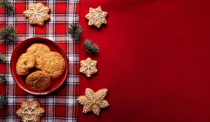 Em cima de uma mesa decorada de Natal, prato com biscoitos redondos e formado de estrelas crocantes, os biscoitos em formato de estrela estão decorados com glacê branco.