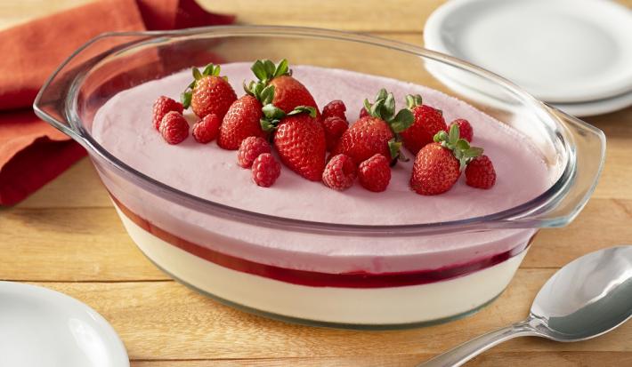 Fotografia em tons de vermelho em uma bancada de madeira marrom. No centro, uma travessa contendo o Creme Chinês. Ao fundo, dois pratos brancos, uma toalha vermelha e uma colher de inox.