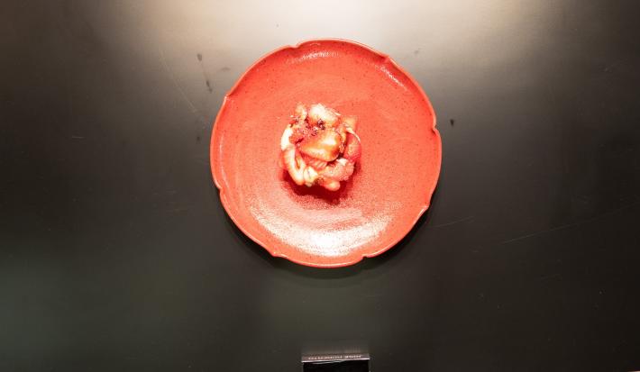 Fotografia vista de cima de um prato em tons de rosa sobre uma bancada preta. Dentro do prato tem uma minitorta de morango com coulis de morango e redução de vinagre balsâmico.