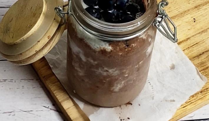 Foto da receita de pudim de chia servida em um pote hermético de vidro sobre uma tábua de madeira em cima de uma mesa de madeira branca.