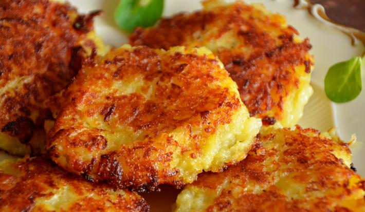 Fotografia em tons de amarelo, laranja e branco com pequenos bolinhos de frango ao centro. Esses bolinhos possuem uma crosta dourada proveniente de seu cozimento e encontram-se brilhantes.