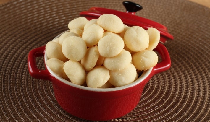Em cima de uma mesa, recipiente redondo com biscoitos amanteigados redondos e dourados.