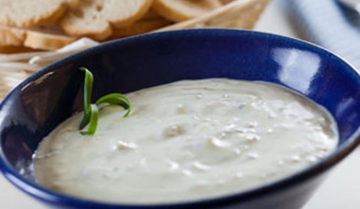 Fotografia em tons de branco e azul, ao centro recipiente de porcelana azul com patê de Gorgonzola, cestinha com torradas ao fundo e ao lado um guardanapo azul claro com listras em azul escuro.