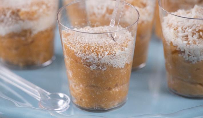 Fotografia em tons de azul com vários potinhos de plástico ao centro. Dentro de cada potinho existe um brigadeiro feito de coco polvilhado com coco ralado.