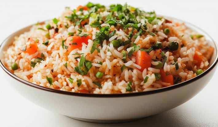 Prato de porcelana branco com arroz soltinho, cenouras cortadas em cubos, ervilhas, decorado com pedaços de salsinha.