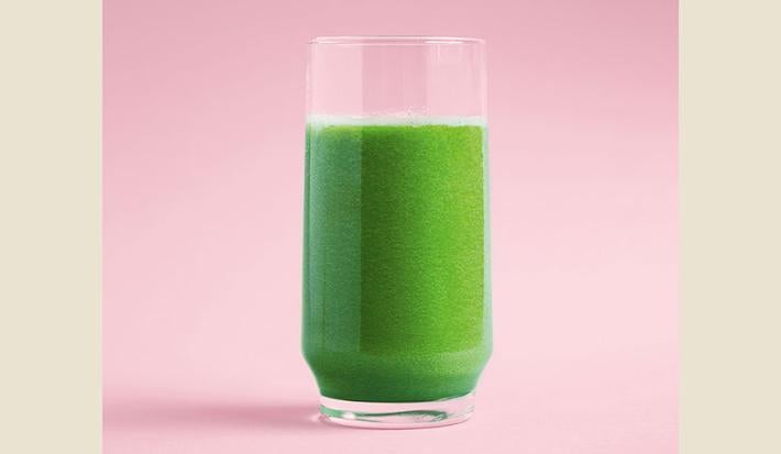 Fotografia em tons de verde e rosa, com copo de suco verde ao centro, em plano rosa.