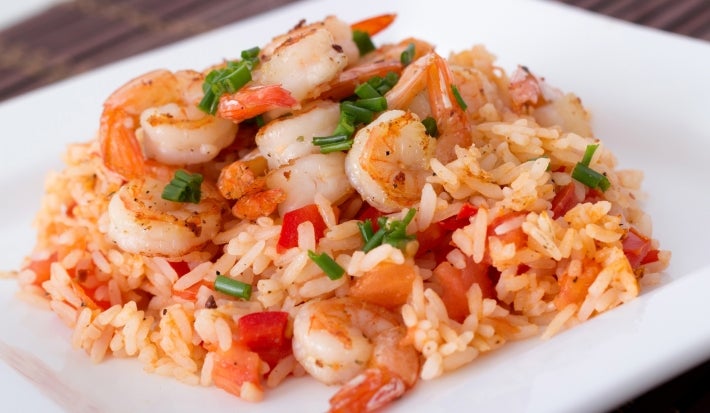 Prato branco quadrado com porção de arroz cremoso e camarão com pimentão vermelho picados.