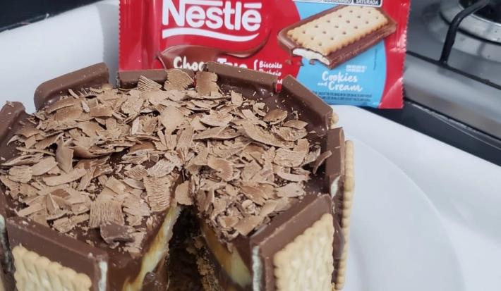 Fotografia de uma torta duo com chocotrio de cookies'n cream com raspas de nestlé classic. A torta está sobre um apoio branco.