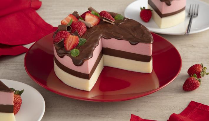Fotografia em tons de vermelho em uma bancada de madeira clara com um prato vermelho ao centro com a torta napolitana cortada ao meio com uma cobertura de chocolate caindo e morangos para decorar. Ao lado, paninhos vermelhos e morangos espalhados na mesa. Fotografia em tons de vermelho em uma bancada de madeira clara com um prato vermelho ao centro com a torta napolitana cortada ao meio com uma cobertura de chocolate caindo e morangos para decorar. Ao lado, paninhos vermelhos e morangos espalhados na mesa.