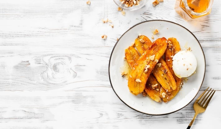 Em cima de uma mesa, prato redondo com bananas fritas, no meio sorvete de coco.