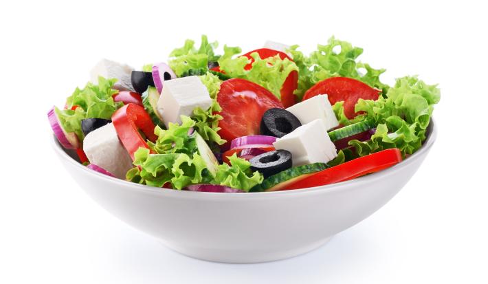 fotografia em tons de branco, verde, vermelho e preto tirada de um recipiente redondo branco com folhas de alface, fatias de tomates, queijo em cubo e fatias de azeitonas pretas.