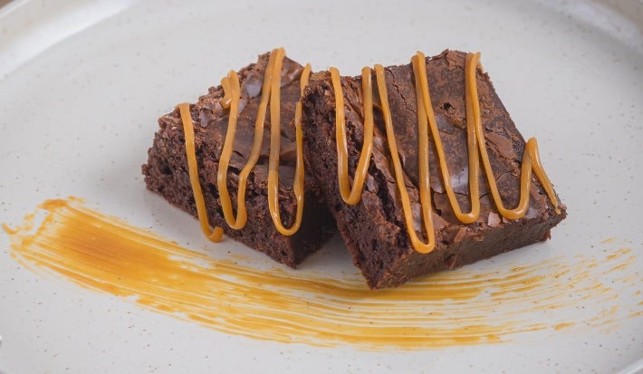 Foto aproximada de duas fatias cortadas da receita de brownie clássico de chocolate, decoradas com fios de doce de leite feito com Leite Moça cozido