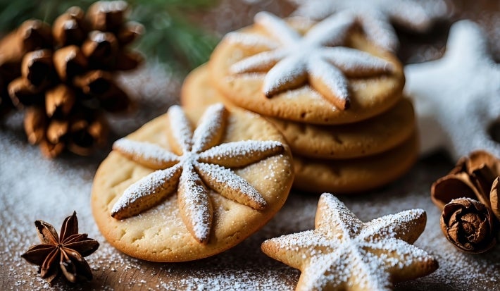 Em cima de uma mesa, prato com biscoito redondo em formato de estrelas, decorado com açúcar de confeiteiro.