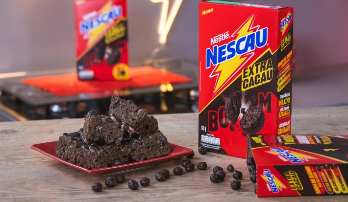 Foto da receita de Delícia Crocante de Chocolate. Observa-se a receita sobre um prato quadrado vermelho e, ao lado direito e atrás, 3 embalagens de NESCAU Cereal Extra Cacau.