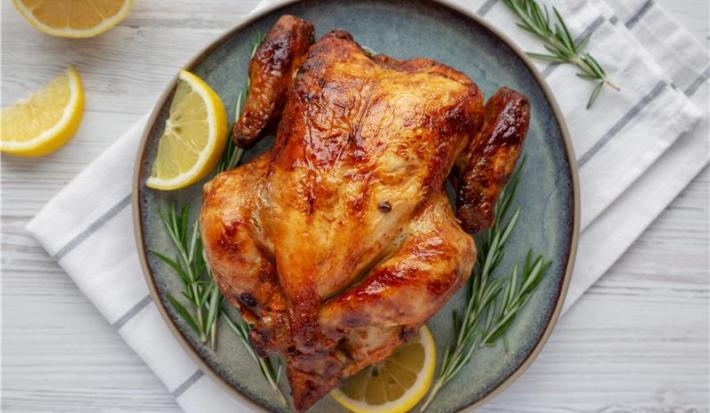 A imagem mostra um frango assado disposto em um prato azul com rodelas de limão e alecrim