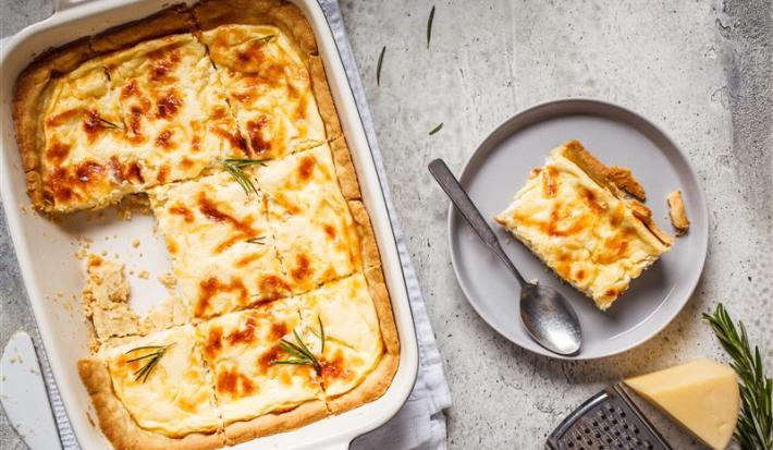 Fotografia mostra uma torta salgada coberta com uma superfície dourada e decorada com ervas frescas.