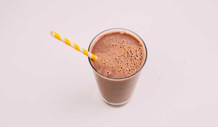fotografia em tons de marrom tirada de um copo transparente, com uma bebida de chocolate gelada e um canudo branco e amarelo para servir.